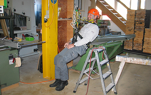 Un collaborateur est suspendu dans le hall de production à un harnais, à 30 centimètres du sol, dans le cadre de la formation.  